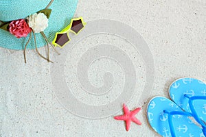 Top view of beach sand with straw hat, sunglasses, slippers and starfish.