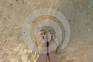top view on beautiful female feet with red pedicure in slates in the water on the sea sand. the concept of relaxation by