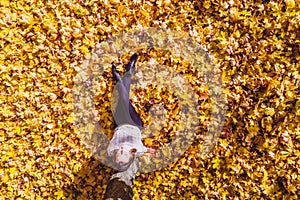 Top view. Beautiful happy young woman sitting under tree and dreaming on the autumn maple leaves in the park. Aerial, drone view.