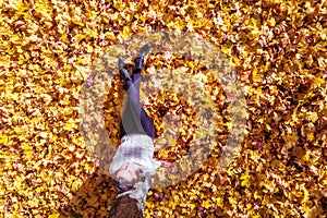 Top view. Beautiful happy young woman sitting under tree and dreaming on the autumn maple leaves in the park. Aerial, drone view.