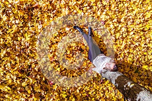 Top view. Beautiful happy young woman sitting under tree and dreaming on the autumn maple leaves in the park. Aerial, drone view.