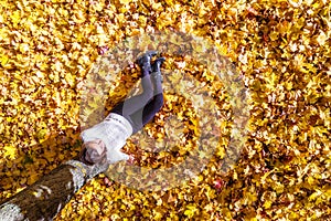 Top view. Beautiful happy young woman sitting under tree and dreaming on the autumn maple leaves in the park. Aerial, drone view.