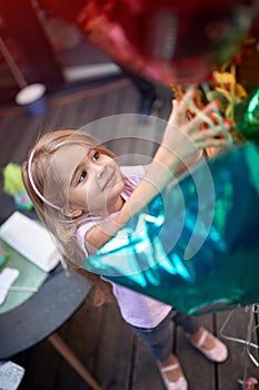 Top view of a beautiful little girl reaching balloons