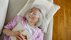 Top view of beautiful mature woman asleep with book. Weekend activity for older woman, relaxing at home.