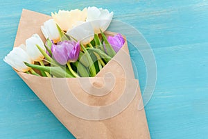 top view of beautiful tulip bouquet in craft paper on turquoise wooden