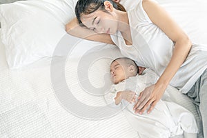Top view of beautiful young Asian mom and her cute little baby sleeping in bed at home