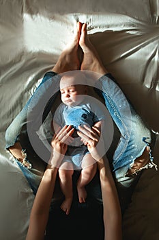 Top view of beautiful young mom and her cute little son lying on white bed linen. Mom holding her sleeping baby`s hands