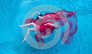 Top view of a beautiful young sexy dark-haired women relaxed in red dress floating weightlessly elegant in the water of the pool,