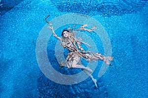 Top view of a beautiful young sexy woman floating swimming elegantly relaxed in dried up leaves of a banana tree, turquoise blue