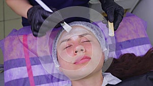 Top view of beautiful young woman getting face skin treatment. Cosmetician is undertaking the procedure applying cream.