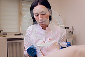 Top view of beautiful young woman getting face skin treatment. Cosmetician is undertaking the procedure applying cream.