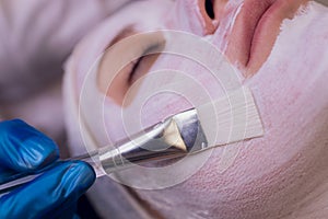 Top view of beautiful young woman getting face skin treatment. Cosmetician is undertaking the procedure applying cream.