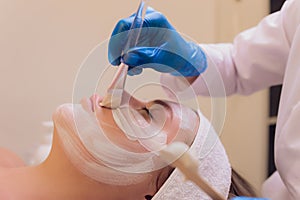 Top view of beautiful young woman getting face skin treatment. Cosmetician is undertaking the procedure applying cream.