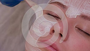 Top view of beautiful young woman getting face skin treatment. Cosmetician is undertaking the procedure applying cream.