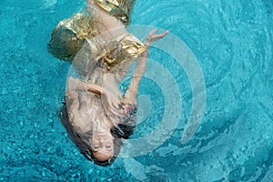 Top view of a beautiful young woman in golden dress, evening dress, towel floats weightlessly elegantly swimming in the water