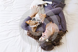 top view of a beautiful young woman lying on bed with her cute small dog besides. Dog wearing bowtie. Home, indoors and lifestyle