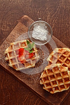 Top view belgian waffles with strawberries on cutting board