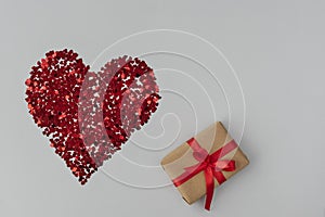 top view of big red heart made from little glittering confeti of heart shapes, gift box with red ribbon is near, photo