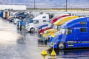 Top view of the big rigs semi trucks with different semi trailers standing in row on the truck stop parking lot waiting for