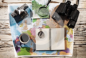Top view of binoculars, compass, retro photo camera, coffee and map on a white wooden table