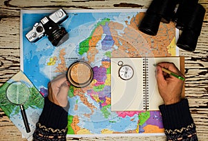 Top view of binoculars, compass, retro photo camera, coffee and map on a white wooden table