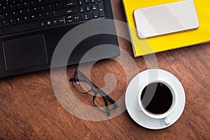 Top view of black coffee with glasses, book, phone and laptop on wooden background