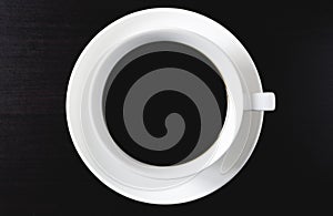 Top view of black coffee in white cup on dark wood flooring