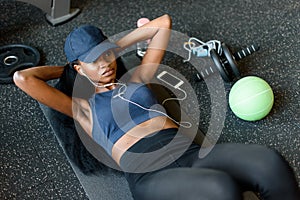 Top view of black fitness instructor doing press ups at the gym and listening to music in earphones