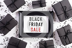 Top view of Black Friday Sale text on white picture frame with black gift box and Christmas ball and berries on white background.