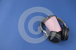 Top view black headphones, smartphone and paper cup coffee on blue background