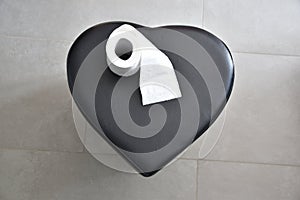 top view of a black heart and toilet paper on a gray background