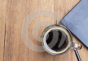 Top view black hot americano coffee in a cup on a rustic wooden table with a book and pencil. Relax and coffee break concept