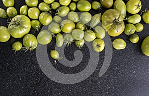 Top view of black kitchen table and green unripe tomatoes harvest on it.Empty space