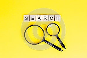 Top view of black magnifying glass with the word search on light yellow background.