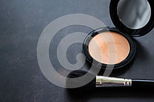 Top view of a black makeup brush and an open box of pink powder with mirror. Black background. Copy space