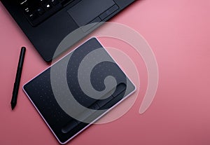 Top view of black pen mouse, digital tablet, and laptop for graphic design work on pink background. Above view of pen graphic