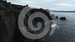 Top view of black rocks with blue waves on cloudy day. Clip. Black stone cliffs on ocean shore on cloudy day. Northern