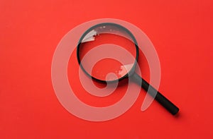 Top view  Black round magnifying glass on red background. used for searching or expanding books.