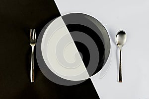 Top view of black and white colors of plate with silver spoon and fork on a black and white background. text space