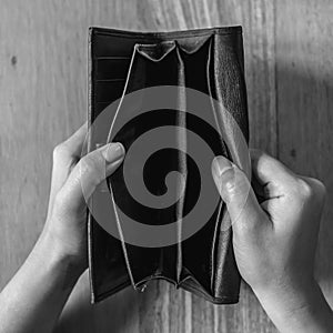 Top view black and white image of woman`s hands open an empty black leather wallet with wooden table