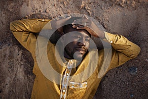 African American Man Lying in Sand and Looking Away Pensively