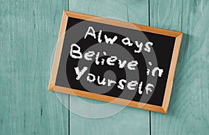 Top view of blackboard with the phrase always believe in yourself, over wooden background