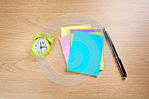 Top view of blank colorful notes paper with pen and alarm clock on background