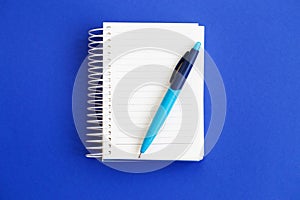 Top view of blank note paper with pen on blue background