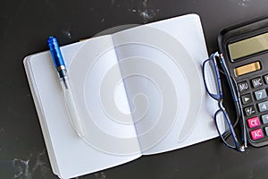 Top view Blank Notebook Calculator and glasses on a black marble table background