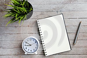 Top view of blank notebook, clock, pen and green plant on wooden pallet background