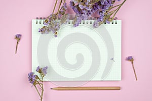 Top view of blank notebook and flower on pink background
