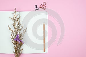 Top view of blank notebook with stationery and flower on pink background