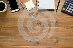 Top view of blank notepad on wooden office desk with smartphone, calculator and coffee cup.