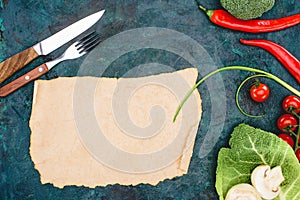 Top view of blank parchment, fork with knife and ripe raw vegetables